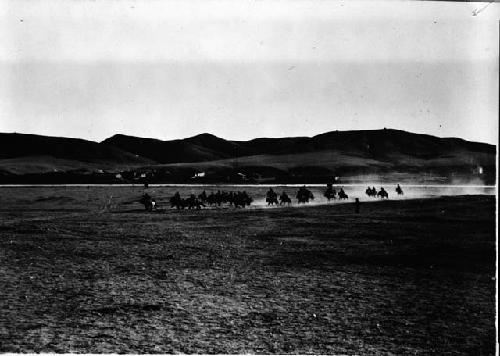 Large group of people riding horses across plain