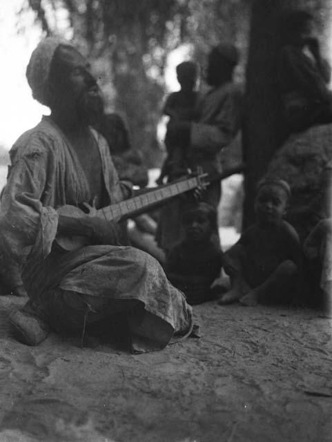 Man sitting, singing, and playing lute-like instrument