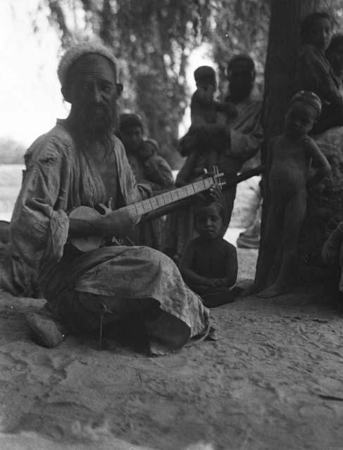 Man sitting, singing, and playing lute-like instrument