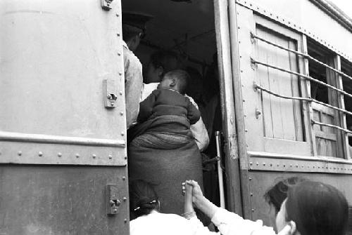 Woman carrying boy on back and others boarding train