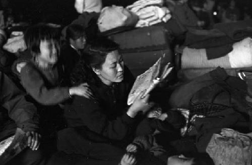 Portrait of woman reading newspaper while baby sits on her back