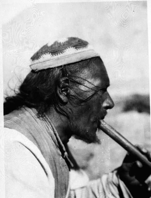 Side-view portrait of man wearing hat and playing flute