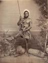 Studio staged bush scene featuring an Aboriginal man holding a spear and a boomerang, wearing white ochre paint
