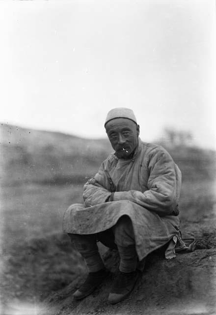 Portrait of a man, seated, wearing white cap