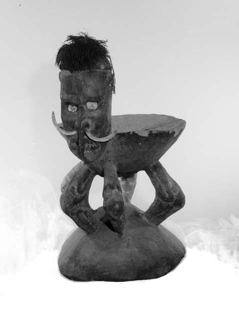 Large painted wooden stool with carved head having boar tusks through nose
