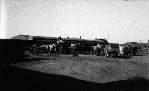 Several carts and horses and people in front of walls