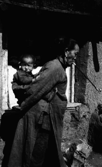 Side-view of woman with long pipe holding baby on her back