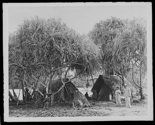 Men in front of huts in jungle setting