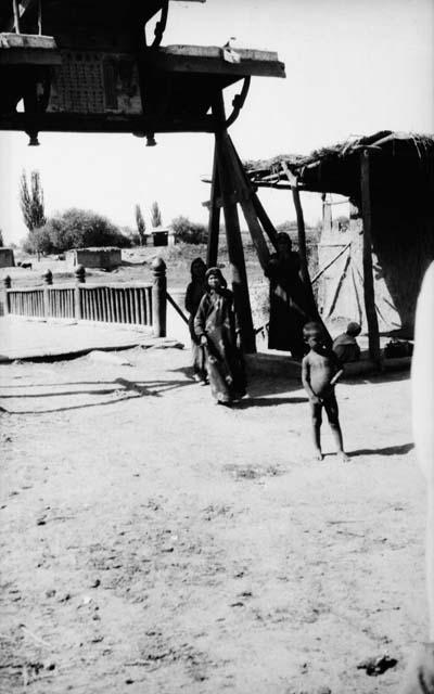 Three women and naked little boy standing by pailou and building by bridge