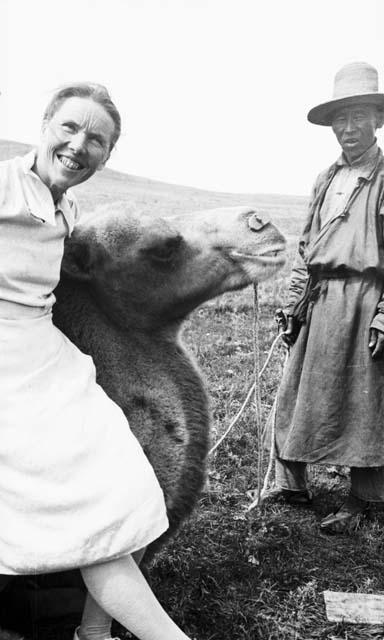 Woman leaning on kneeling camel, man standing by