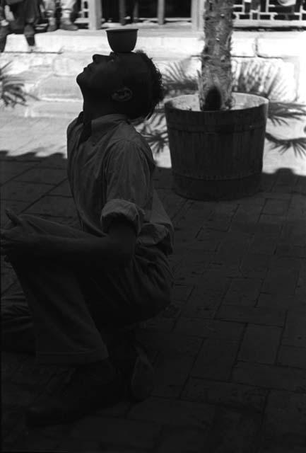 John K. Fairbanks, kneeling on terrace with cup on forehead