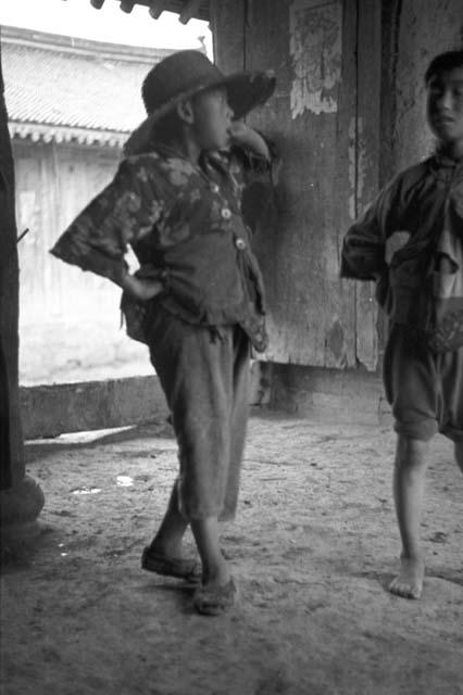 Two children standing on dirt floor, wall and building behind