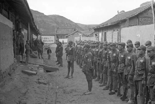 Two rows of soldiers, buildings and wall with Chinese characters in background