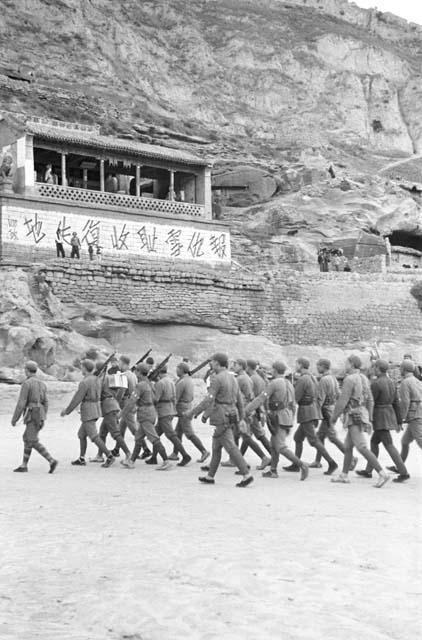 Group of soldiers marching, building built in cliff in background