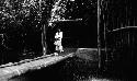 Boy and man at end of bridge in front of building set in trees