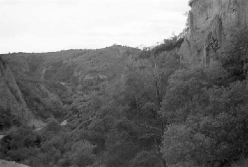 Road through steep hills, trees in foreground