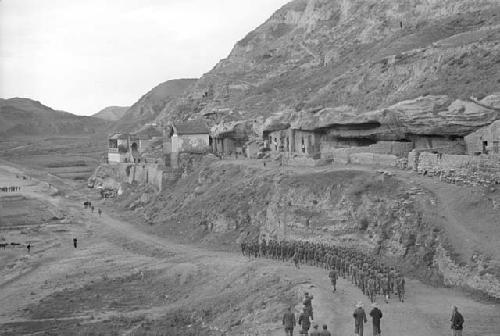 Long line of soldiers marching down road along the edge of a steep hill