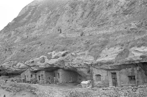 View of several small mud brick buildings built into side of cliff