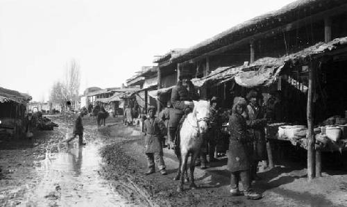 Street in Chuguchak, man on a horse, and several men standing in front of a mark