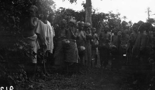 Women and men on rural road in jungle, carrying bundles in nets