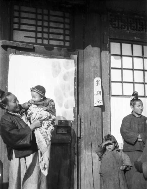 Two women, one holding a baby, the other a small girl standing by her