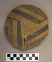 Base fragment of black on yellow pottery bowl roughly circular in form but edges