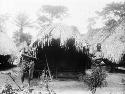 Two women nursing babies, standing in front of hut, Sapo, Pudu clan