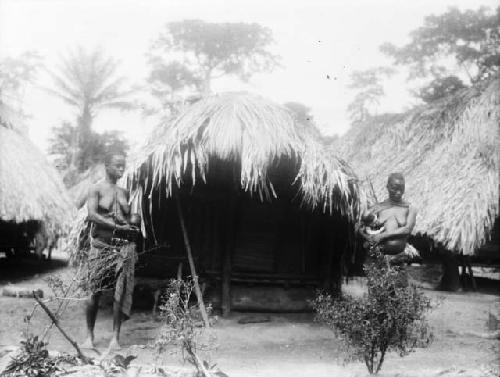 Two women nursing babies, standing in front of hut, Sapo, Pudu clan