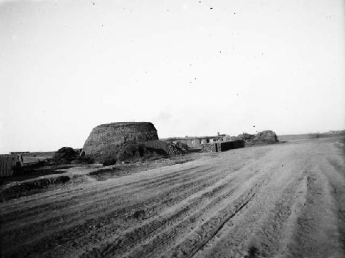 Plowed field with large kiln and small hut in background, large piles of bricks