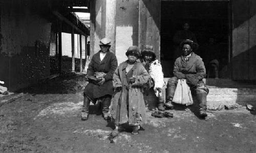 Turk in village, three men sitting and one boy standing in front of a building