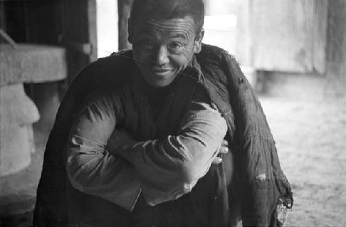 Portrait of man with closely-cropped hair, squatting with arms around knees