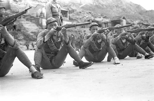 Close-up of young soldiers drilling with rifles. Cliff in background