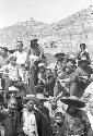 Crowd of men and boys sitting on hillside. Mountains in distance