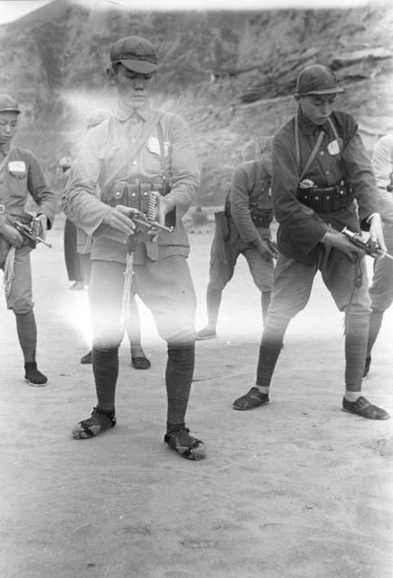 Close-up of two young soldiers drilling with handguns. Cliff in background