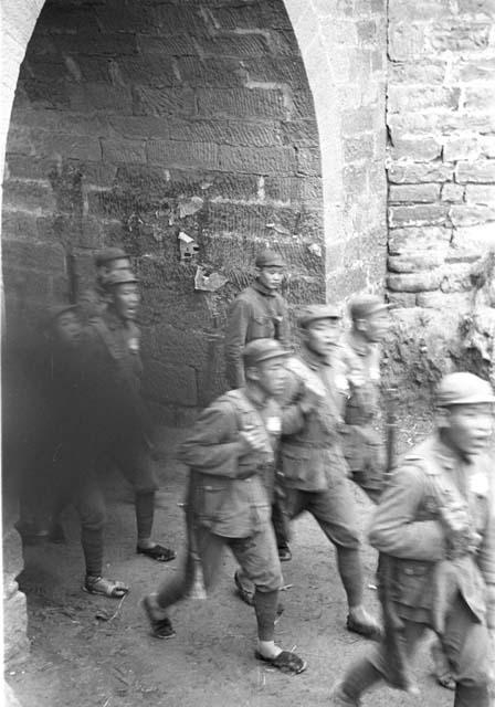 Close-up of group of soldiers marching under city gate