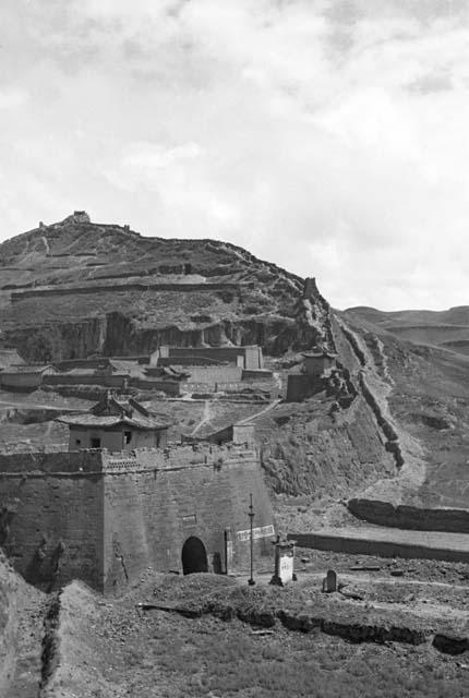 Buildings and walls built into hillside. Sign in front of largest building