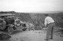 Car on road at edge of huge canyon. Man leaning over facing car