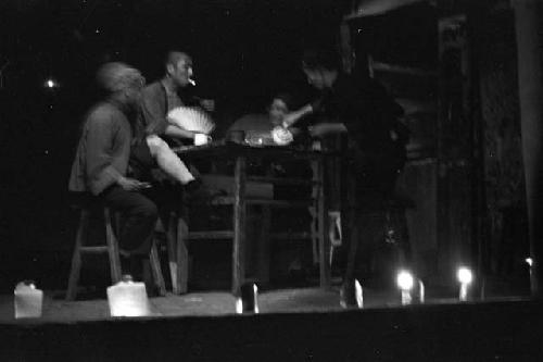 Stage lit by candlelight, actors sitting around a table