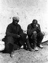 Chugachak, two men sitting on log in front of wall