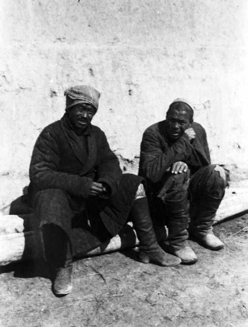 Chugachak, two men sitting on log in front of wall