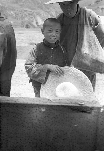 Child holding and adult wearing wide-brimmed hats. Hills in background