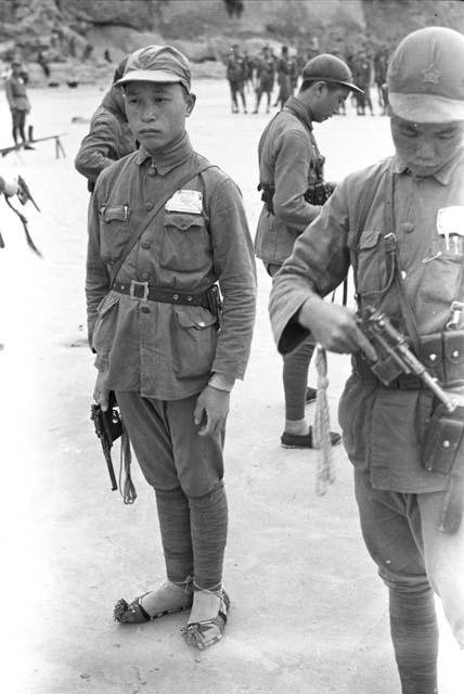 Close-up of two young soldiers drilling with handguns. Cliff in background