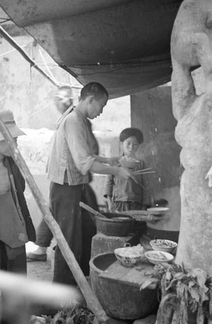 Man at food stall preparing bowl of noodles