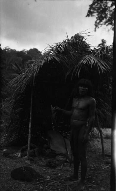 Man standing beside palm leaf structure
