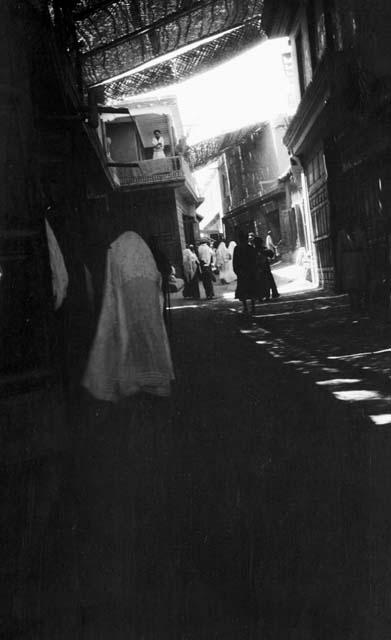 Shop and crowd in covered street, man on balcony