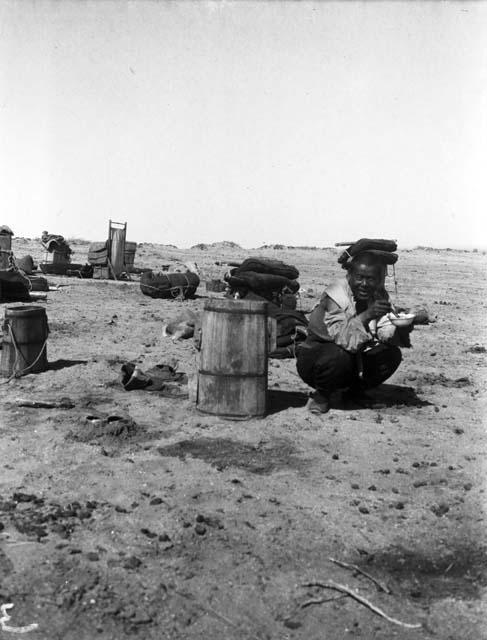 Moses crouched with water buckets and other camp equipment in background