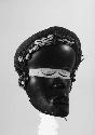 Black wooden mask adorned with shells, beads, and cloth. Gba Glu
