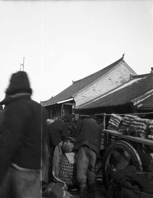 Several people standing next to cart piled up with macaroni