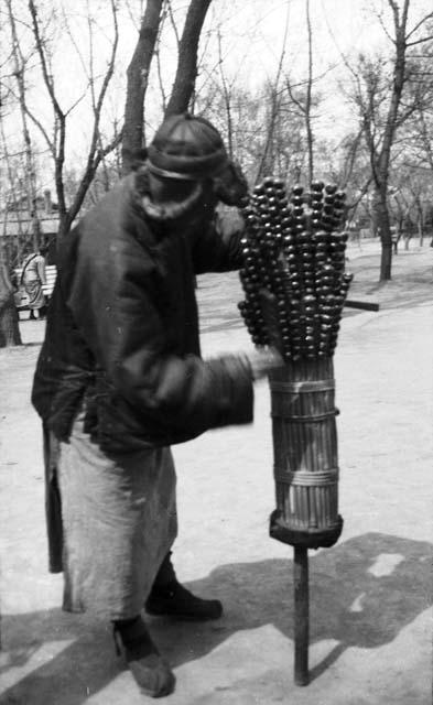 Peddler selling skewers of candy coated crab apples stuck in a stand