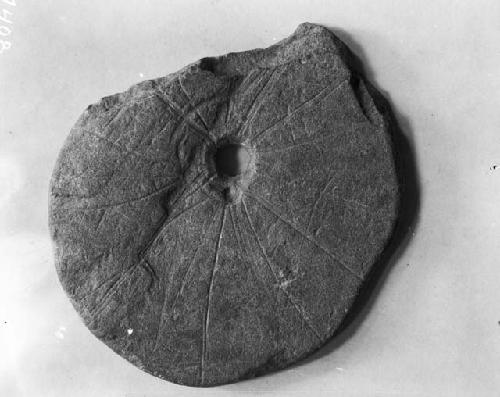 Incised dish-like, perforated stone, circular lines projecting out from center